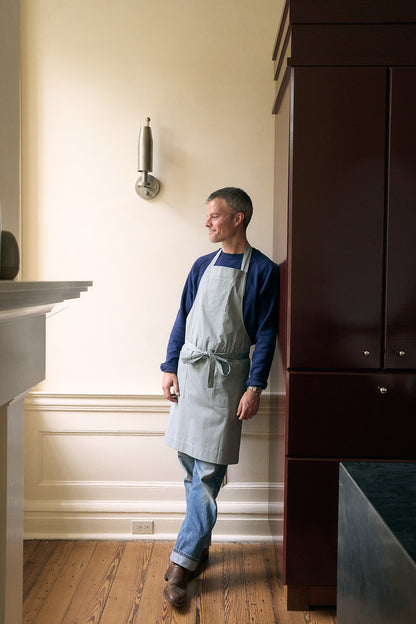 a man wearing a grey apron leaning against a wall